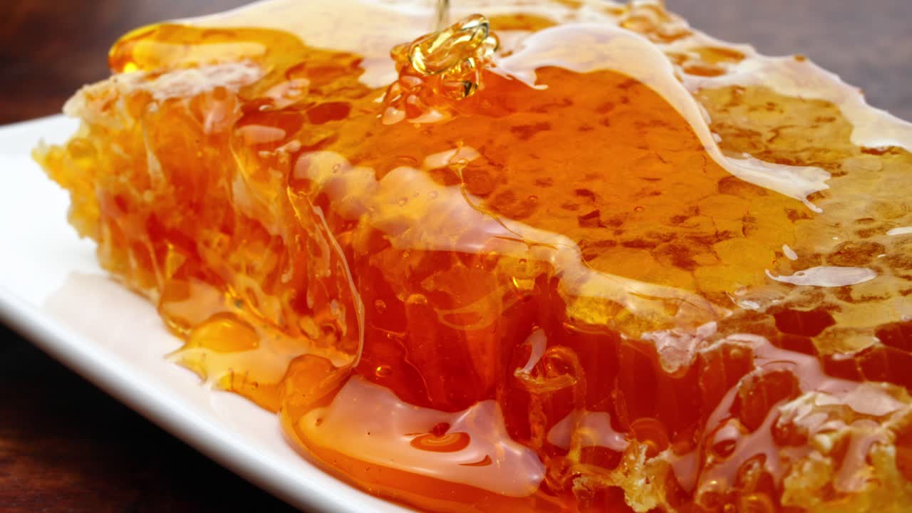 食欲をそそるマクロのフードコンポジションで蜂蜜に覆われたお皿に、ハニカムスライスが乗っており、蜂蜜が滴り落ちています。