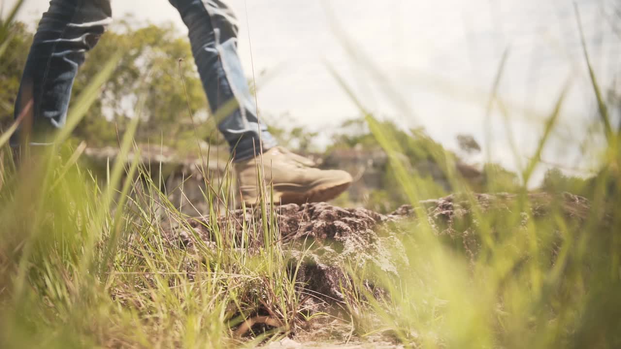 una persona con jeans azules y botas de montaña caminando de un lado a otro por un camino de tierra en un día soleado
