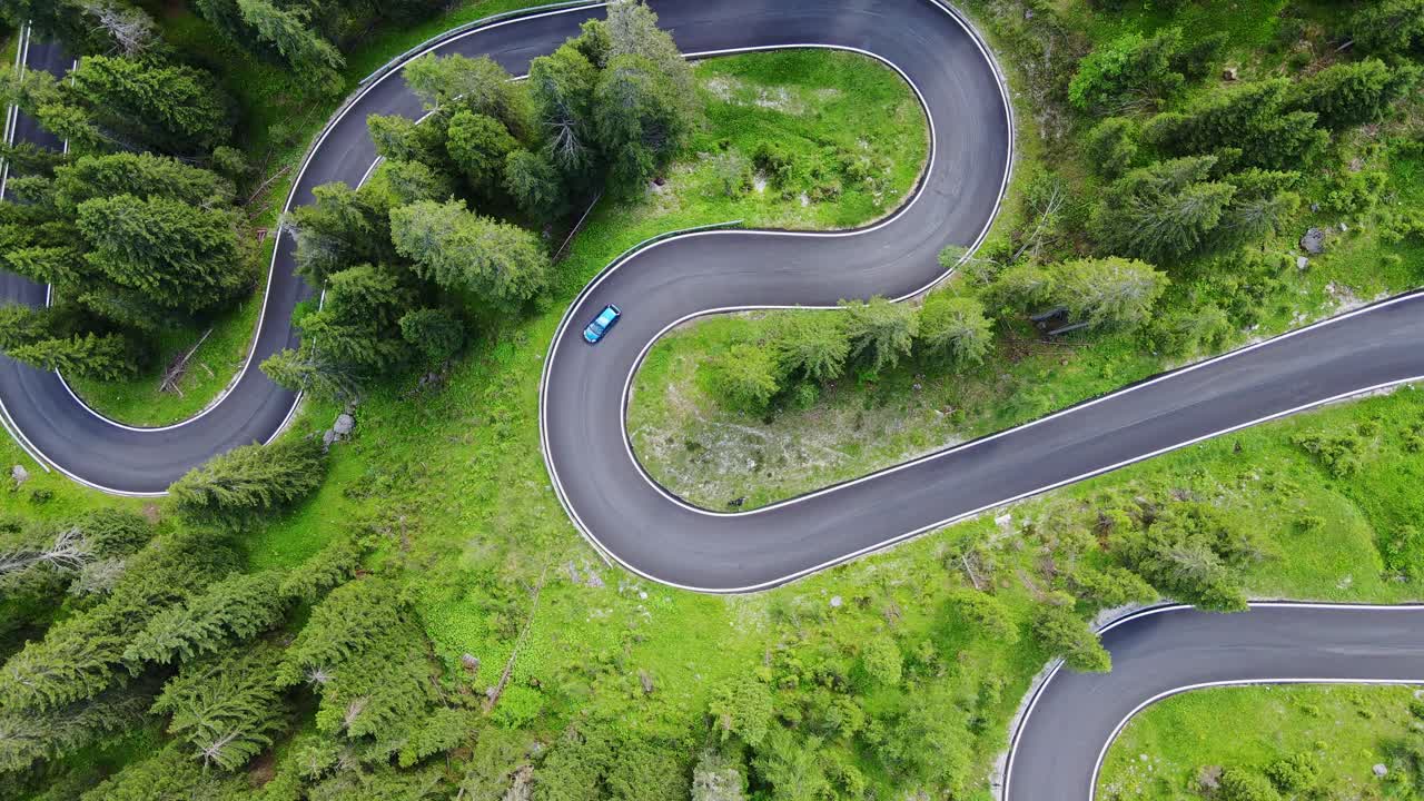 Top down drone of green car driving uphill on winding Passo Giau mountain road