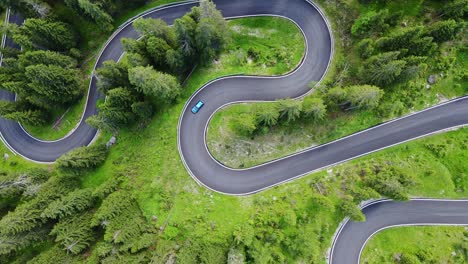 top down drone of green car driving uphill on winding passo giau mountain road
