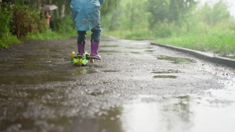 kid finds solace in ride against rainy day small child presses forward on three wheeled scooter with