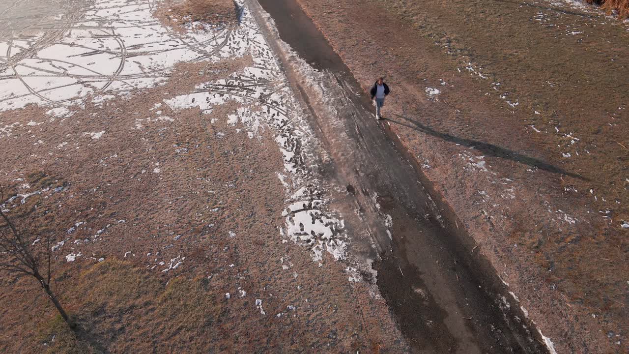 Diagonal aerial shot of a man running on a winter sidewalk near a lake.