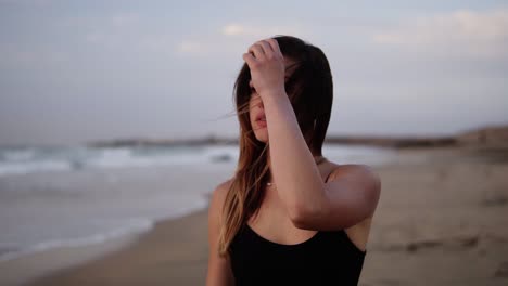retrato en primer plano de una mujer joven caminando y mirando la puesta de sol en la playa de arena. chica bonita caminando hacia el océano. concepto de feminidad. viento agitando su cabello