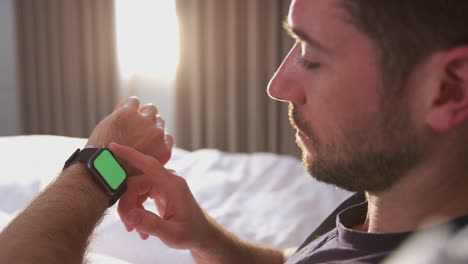hombre sentado en la cama mirando la pantalla de un reloj inteligente