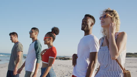 group of young adult friends walking on a beach talking 4k