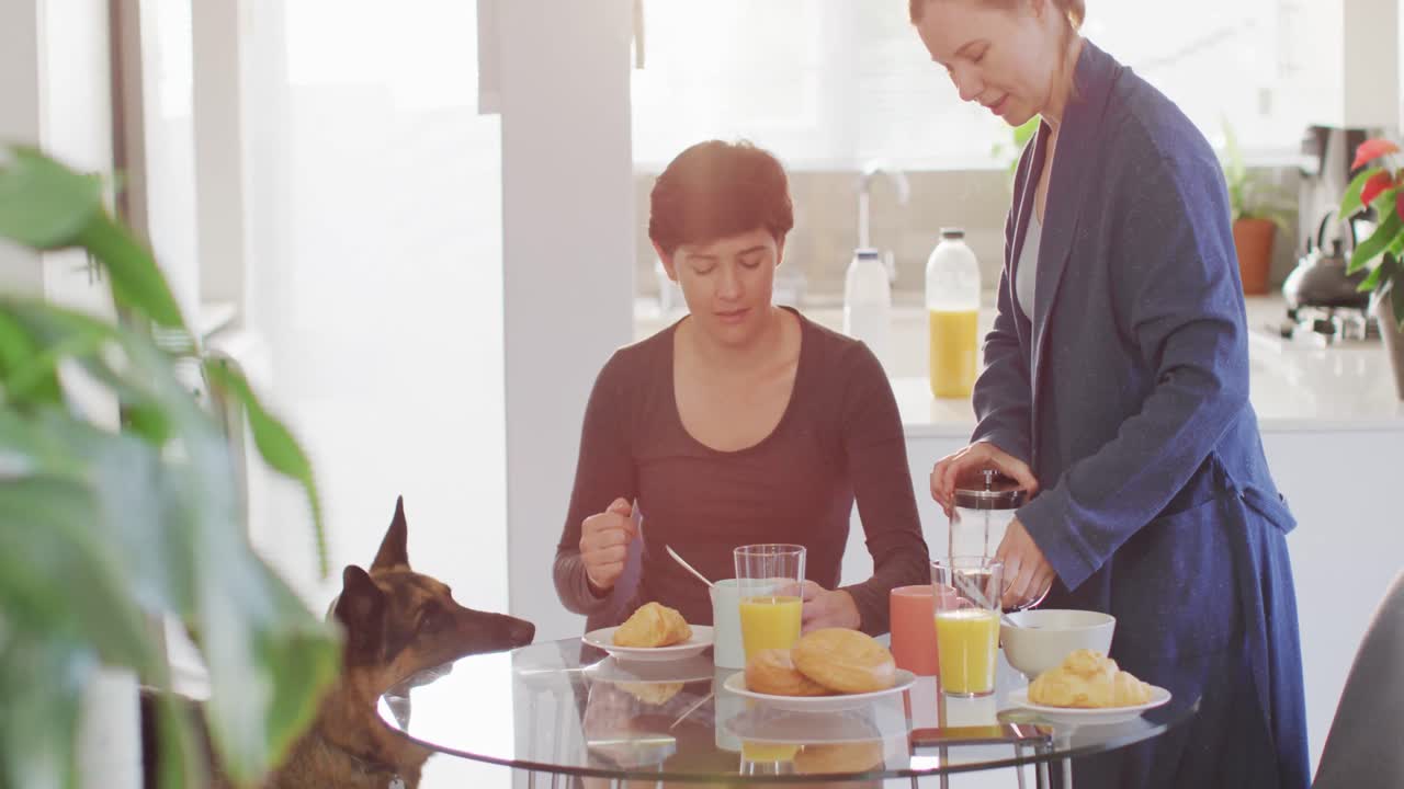 하색 레즈비언 커플이 집의 거실에서 함께 아침을 먹고 있습니다.