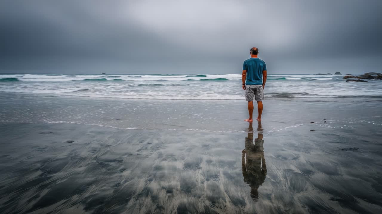 Una figura solitaria contempla le onde dell'oceano sotto un cielo grigio, riflettendo pensieri ed emozioni profonde mentre si trova sulla riva.