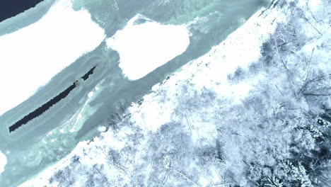 aerial top down view of winter wonderland with frozen lake and forest