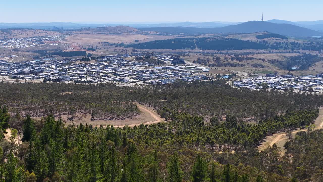 Szerokie ujęcie panoramiczne przesuwa się po dzielnicach mieszkalnych i zalesionych wzgórzach Canberry w Australii