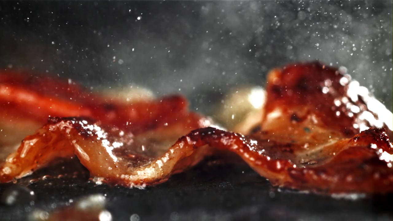 Nærbillede af bacon, der steger og syder på en varm pande