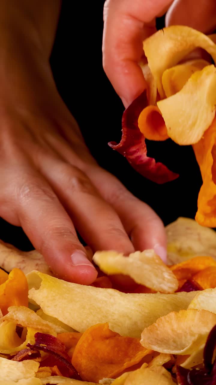 Hand reaches into colorful pile of crispy root vegetable chips, dramatic lighting, close-up view