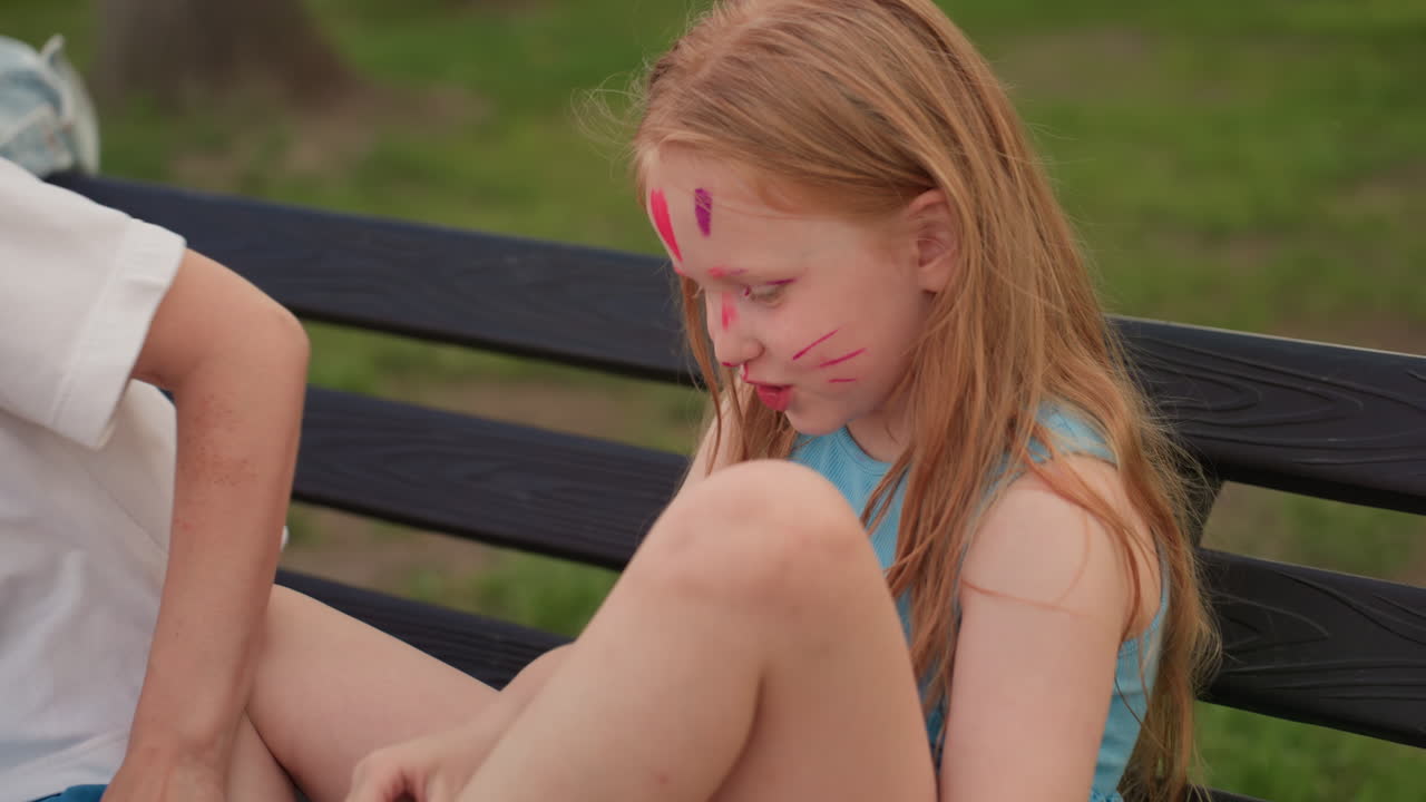 youngster seated on bench smiling as mother helps put sock on foot during playful park outing, warm summer light, green background, close connection and gentle care between parent and child