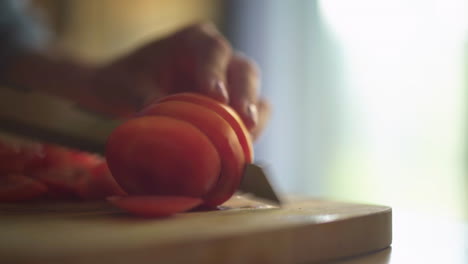 cerca de la mano de una mujer cortando un tomate