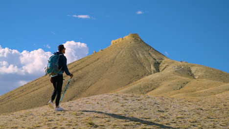 a tourist treks toward ancient dry hill pyramid in upper mustang nepal carrying a stick and bag full of excitement and adventure