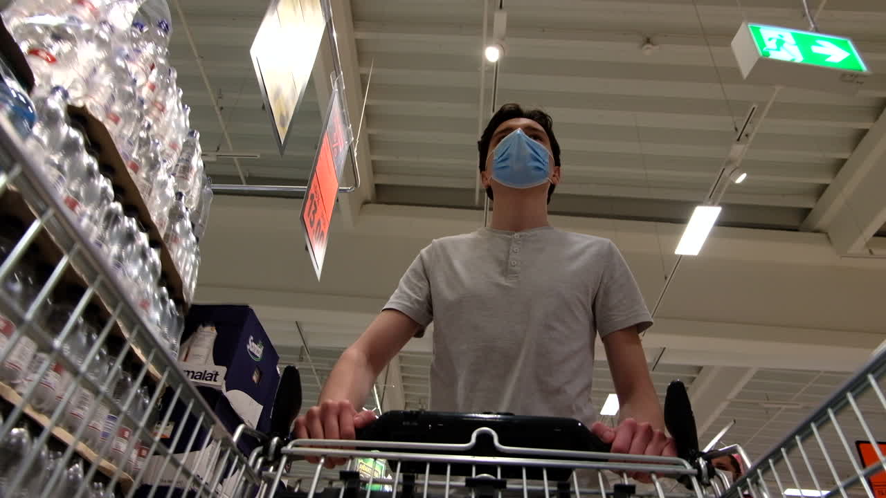 CHISINAU, MOLDOVA - JUNE 5, 2020: Young man with a protective medical mask walking in a supermarket and looking around. View from the cart. Corona Virus idea