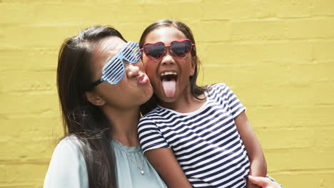 biracial mother and daughter posing having fun against yellow background outdoors