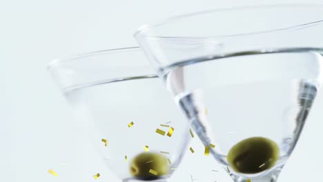 Animation-of-confetti-falling-over-cocktail-glasses-with-olives-on-white-background