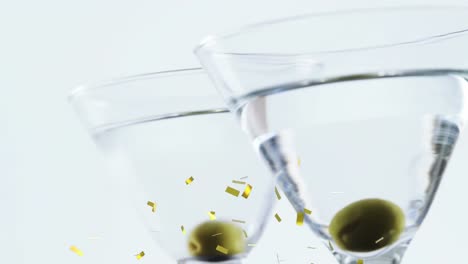 animation of confetti falling over cocktail glasses with olives on white background