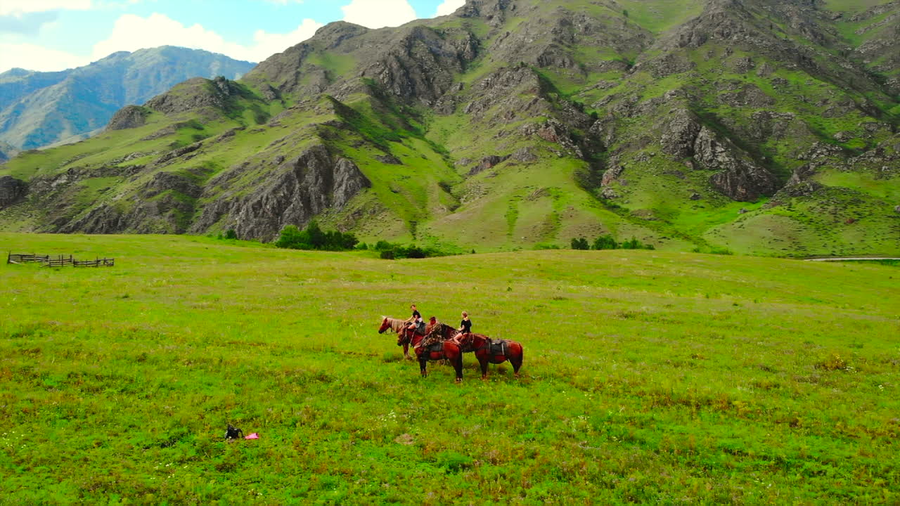 People riding horses in a green field with mountains in the background