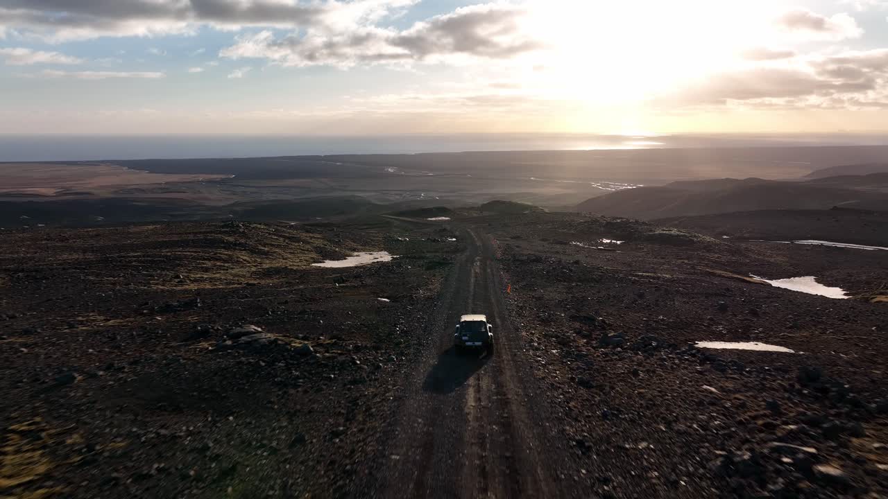 SUV driving on a remote dirt road through a rugged landscape at sunset