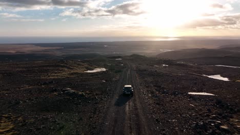 suv driving on a remote dirt road through a rugged landscape at sunset