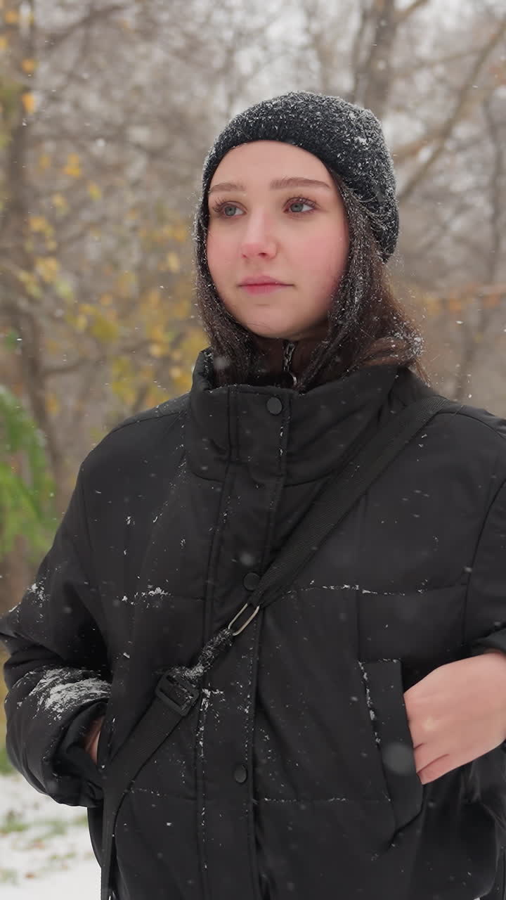 chica con capucha negra ajustando su guitarra en su mochila, mirando a su alrededor pensativo, con un banco cubierto de nieve en el fondo en medio de un sereno paisaje nevado