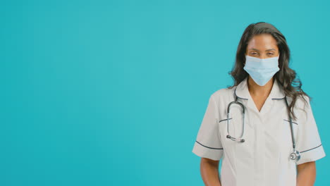 portrait of female nurse in uniform wearing face mask standing in front of blue studio background