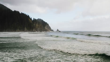 shallow waves of pacific ocean roll into protected cover along oregon coast while surfers try to catch a wave