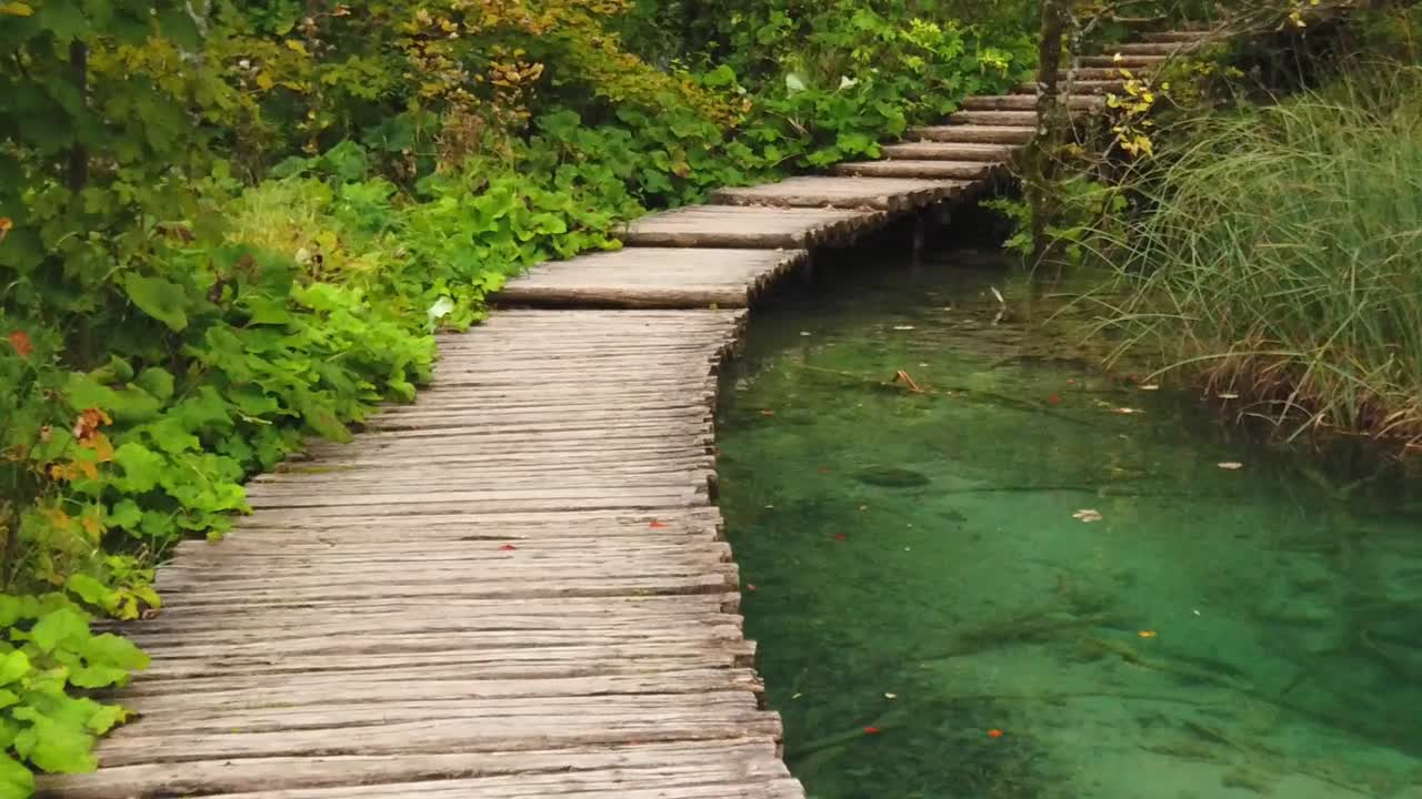 camine a cámara lenta a lo largo de un paseo marítimo de madera sobre una piscina de agua turquesa que fluye en el parque nacional de los lagos de plitvice en croacia, europa