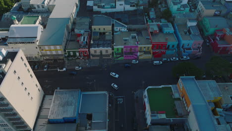 Blick-Aus-Der-Vogelperspektive-Auf-Fahrzeuge,-Die-An-Einer-Straßenkreuzung-In-Der-Stadt-Vorbeifahren.-Bunte-Häuser-Im-Wohnviertel-Bo-Kaap.-Kapstadt,-Süd-Afrika