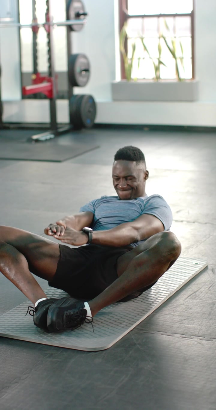 Vertical video: African American man performing opening stretch and overhead reach on mat at gym
