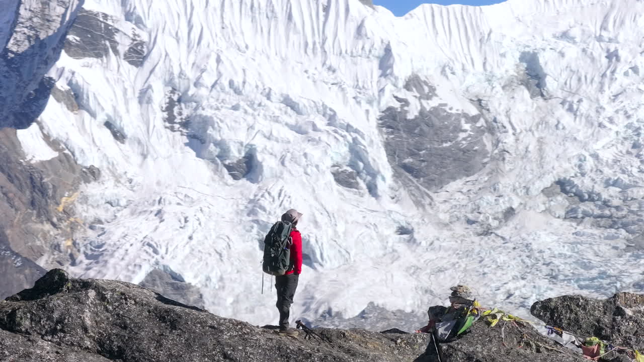 Un turista osserva ghiacciai innevati e vette himalayane bianche nella regione del Khumbu in Nepal. Paesaggio d'alta quota che mostra superfici glaciali e un terreno montuoso aspro.
