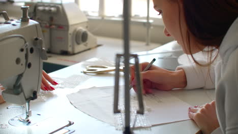 close up of two young women working as fashion designers and drawing sketches for clothes in atelier