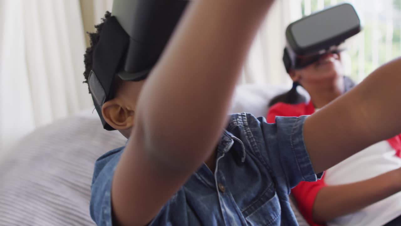 Ragazzo e ragazza multietnici seduti sul divano di casa che giocano indossando occhiali per la realtà virtuale.