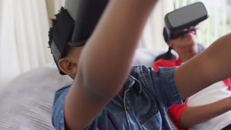 Diverse-boy-and-girl-sitting-at-home-on-sofa-playing-wearing-virtual-reality-glasses