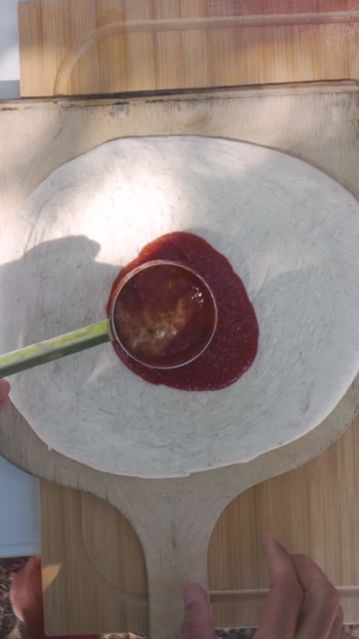 Neapolitan pizza sauce spreading in open-air kitchen with wooden peel, vertical angle highlights artisan rhythm