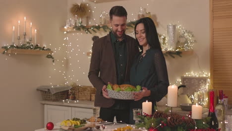 pareja elegante poniendo pollo asado en la mesa de la cena de navidad y luego besándose