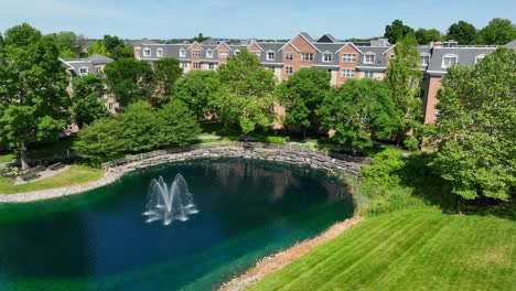 Vista-De-Drones-De-Complejos-De-Apartamentos-Que-Rodean-Un-Entorno-Tipo-Parque-Con-Un-Pequeño-Lago-Con-Una-Fuente.