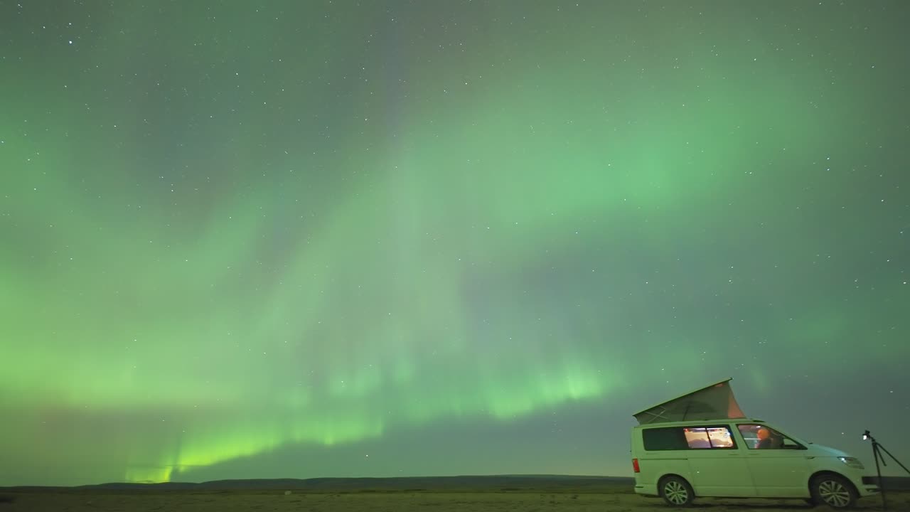 una pequeña furgoneta con una tienda de techo abierta bajo los magníficos cielos de la aurora