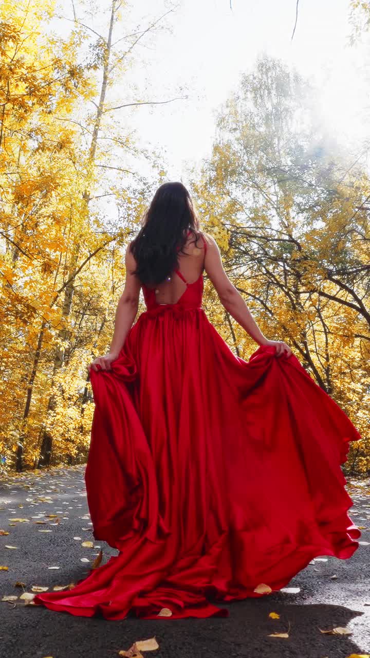 A Captivating Elegance: A Woman in a Flowing Red Dress Stands Gracefully Amidst Golden Autumn Foliage, Embracing the Beauty of Nature and Fashion in Harmony