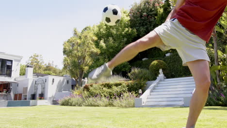 focused biracial man practicing football skills in sunny garden, copy space, slow motion