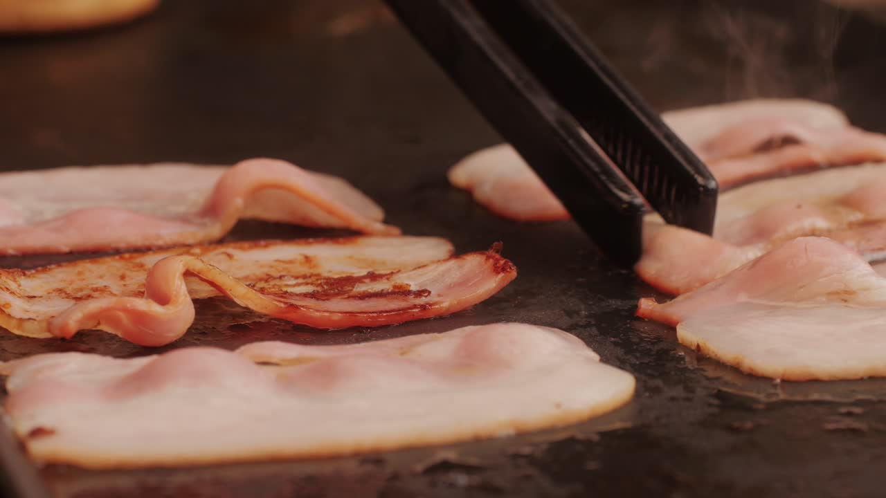 Cooking bacon slice for burgers on the grill close-up macro. The chef in kitchen of the restaurant making cutlets for smash burgers - smash burger beefsteak. Fast and street food concept. High quality 4k footage