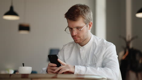 Attraktiver-Mann-Mit-Brille,-Der-Allein-Im-Innenbereich-Steht-Und-Sein-Smartphone-In-Den-Händen-Hält-Und-Die-Nummer-Auf-Dem-Touchscreen-Wählt.-Fröhliche-Junge-Frau,-Die-Auf-Der-Website-Zum-Surfen-Im-Internet-Surft,-Wählt-Das-Online-Konzept-Für-Den-Kauf-Von-Waren