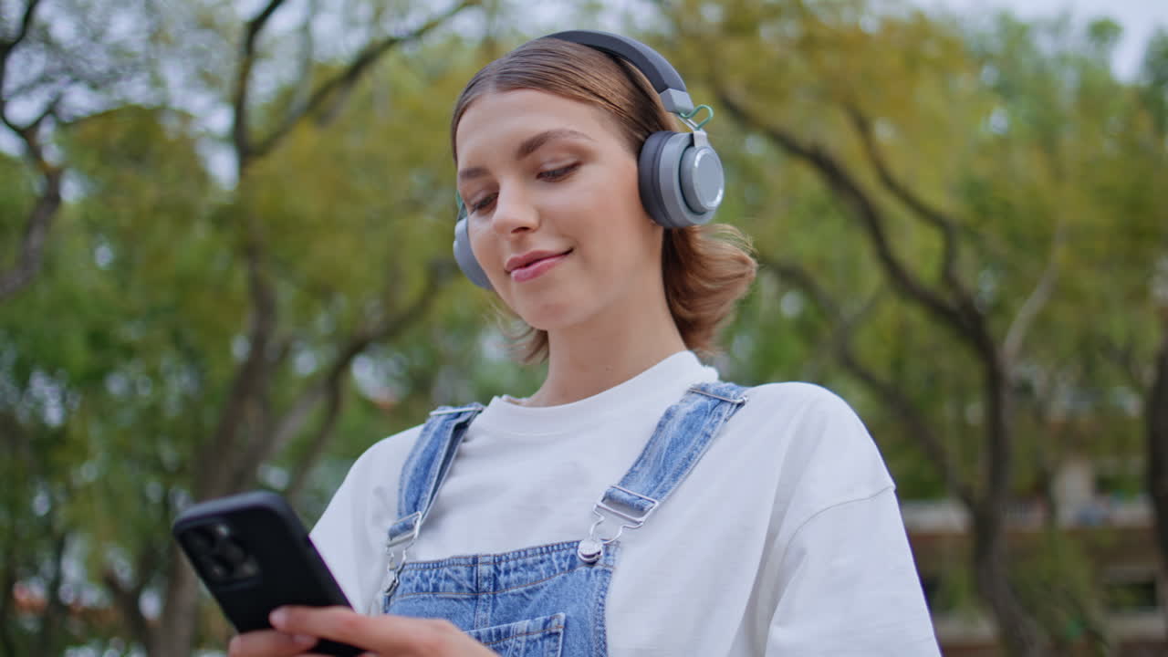 Earphones woman browsing smartphone app at green park closeup. Carefree female