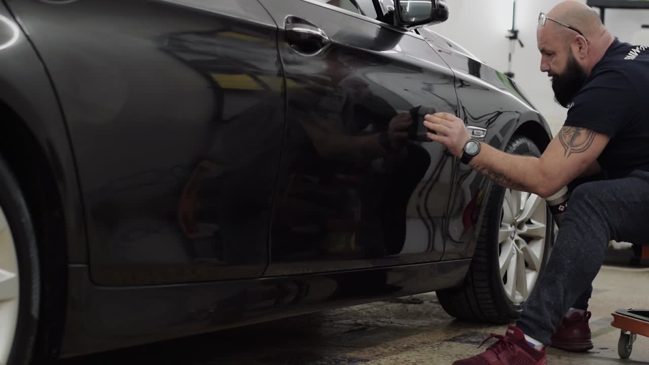 SLOW MOTION car cleaning professional applies product to car door.