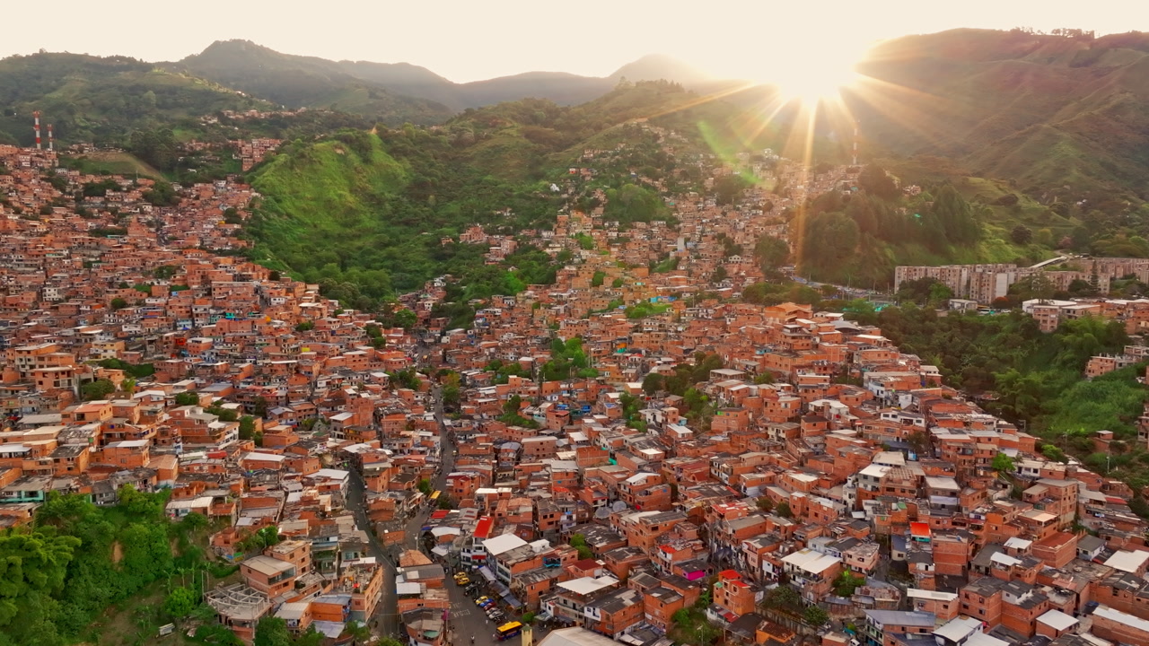 Drone view of Medellin, Colombia at sunset, capturing a sweeping city panorama with warm light, deep shadows, and surrounding peaks.