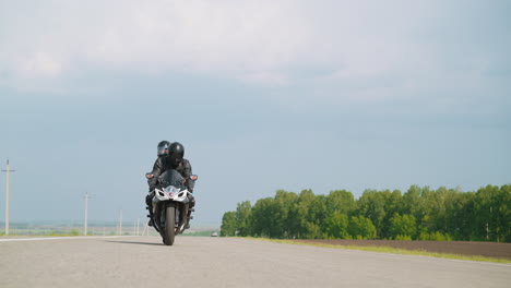 people with helmets ride fast motorcycle along rural road