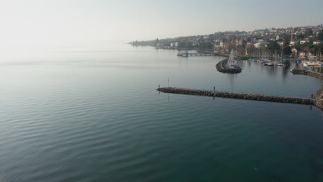 Flying-over-woman-standing-on-end-of-quay-in-beautiful-coastal-city