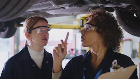 female tutor with student looking underneath car on hydraulic ramp on auto mechanic course