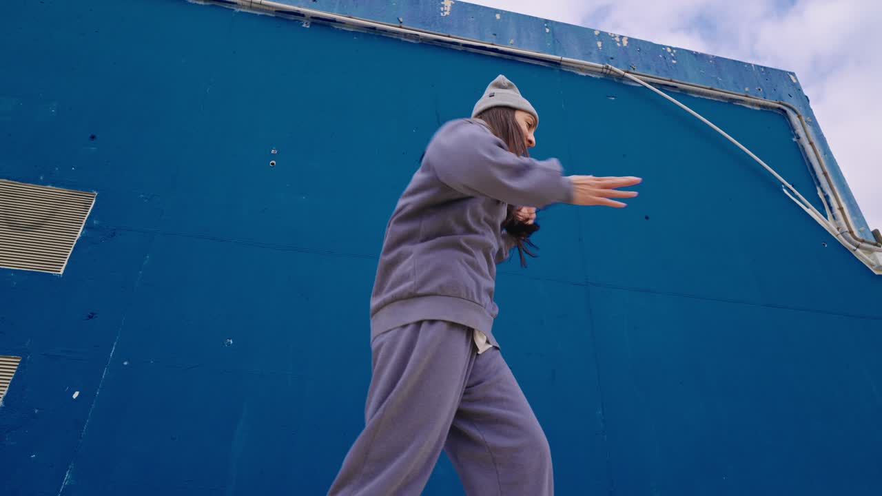 Woman in sweatsuit dancing against a blue wall
